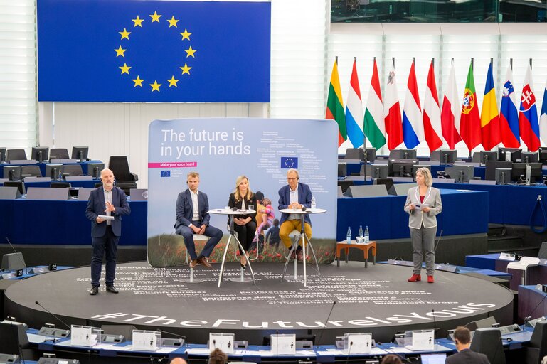 6 people standing on a stage at the CoFoE panel 4, in the background an EU Flag, and a sign saying: the future is in your hands